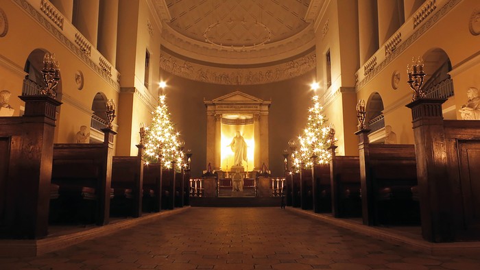 En lysset kirkeinterior med høje kolonner og en central altertavle.