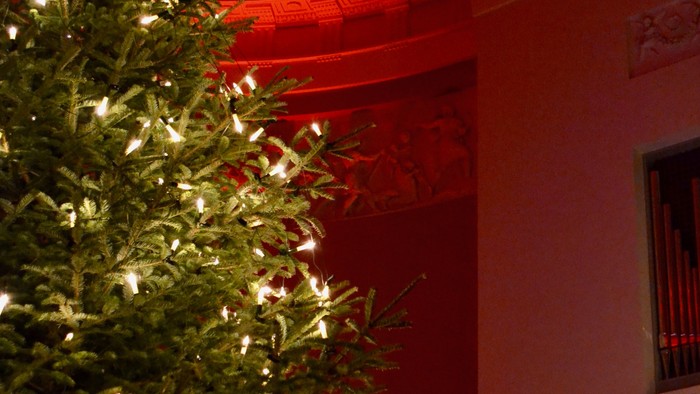 En juletree med lys og pynt i et rum med røde og gule detaljer.