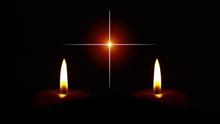 Two lit candles flank a glowing cross against a dark background.