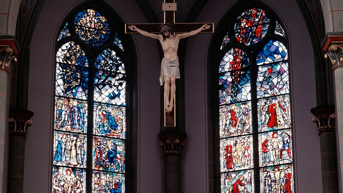 Das Bild zeigt ein Kirchenfenster mit einer Darstellung des Gekreuzigten und farbenfrohen Glasmalereien.