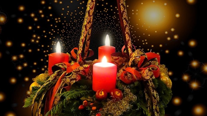 Ein Adventskranz mit vier brennenden Kerzen vor einem funkelnden Hintergrund