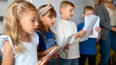 Kinder, die Papiere halten und sich auf eine Aufführung oder Lesung im Klassenzimmer vorbereiten.