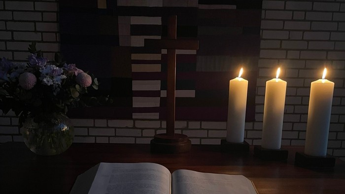 Offene Bibel bei Kerzenlicht vor Kreuz