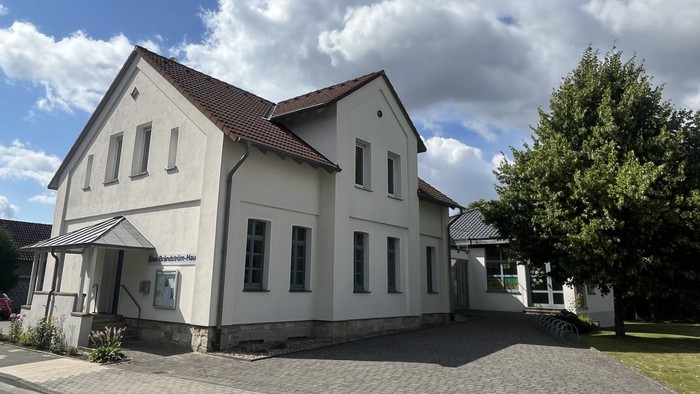 Das Bild zeigt das Laggenbecker Gemeindehaus, ein weiß verputztes Gebäude mit einem Anbau rechts.