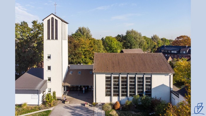 Moderne Kirchenanlage mit hohem Glockenturm, umgeben von üppigen grünen Bäumen und herbstlichem Laub.