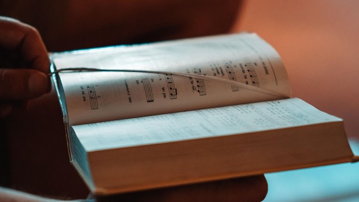 Eine Hand hält ein aufgeschlagenes Buch mit Notizen.