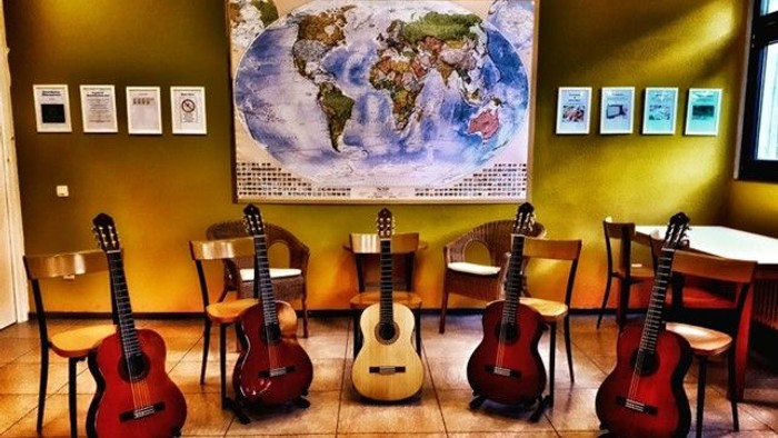 Mehrere Gitarren stehen vor einer Weltkarte und Stühlen