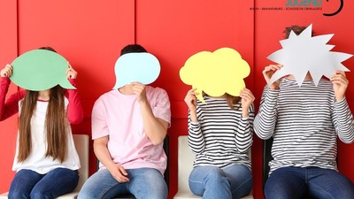 Vier Personen sitzen vor rotem Hintergrund, jede hält ein buntes Pappkopfteil vor ihr Gesicht.