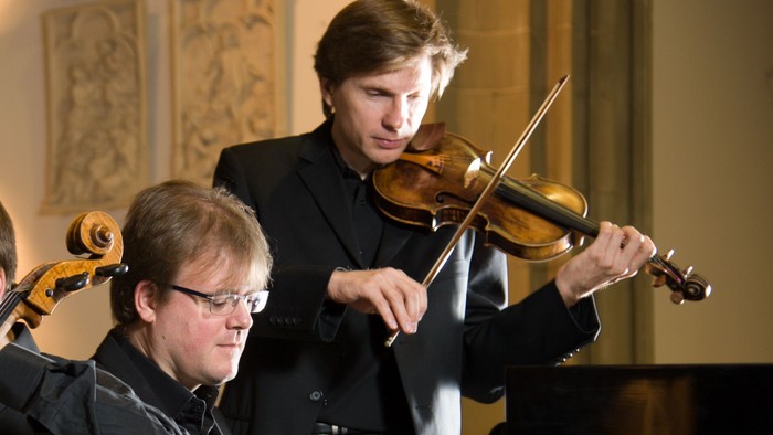 Drei Musiker spielen Cello, Klavier und Geige in einem Konzertsaal
