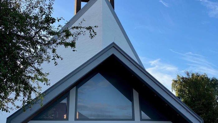 Kleine Kirche mit Glocke und großen Fenstern vor blauem Himmel