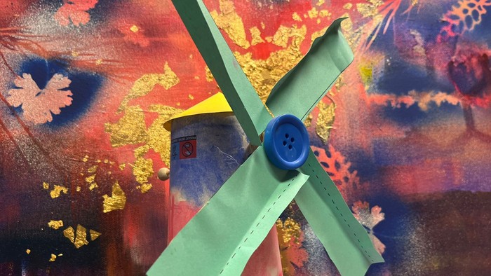 Eine grüne Windmühle mit einem blauen Knopf vor einem bunten Hintergrund.