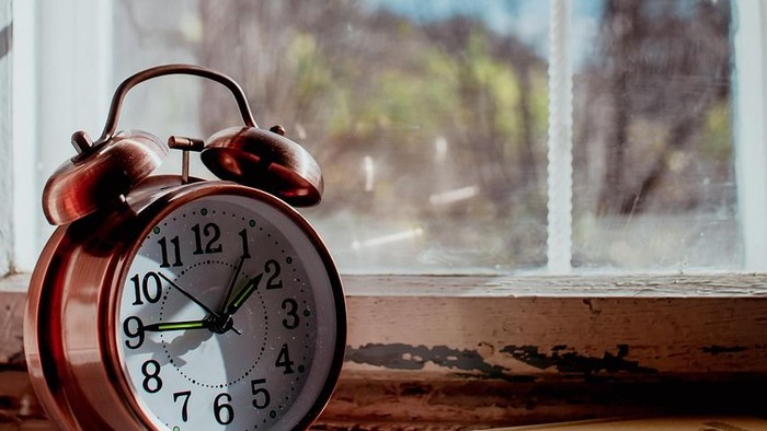 Wecker auf einer Fensterbank mit einem Buch und Blick aus dem Fenster