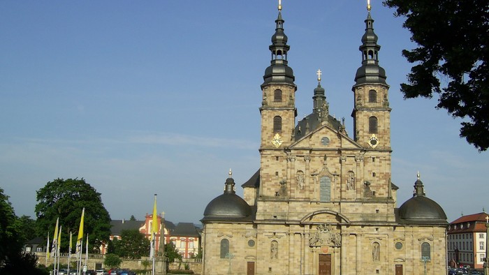 Große Barockkathedrale mit Zwillingstürmen und Kuppeln vor einem klaren blauen Himmel.
