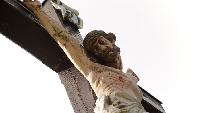 Statue des gekreuzigten Jesus Christus mit detailliertem Gesicht und Händen vor klarem Himmel.