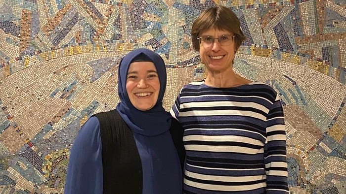 Zwei Frauen lächeln vor einem Mosaik-Wandbild