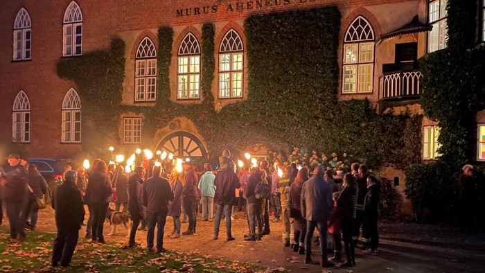 Gruppe von Menschen mit Fackeln vor altem Gebäude