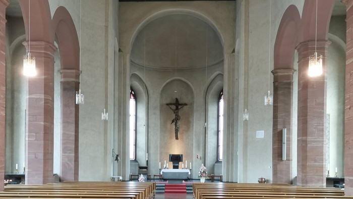 Innenraum einer Kirche mit Holzbanken und Kreuz am Altar
