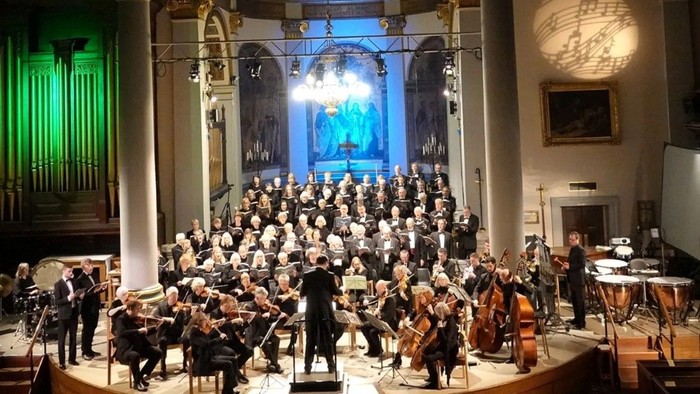 Large orchestra performing in grand church with choir and audience.