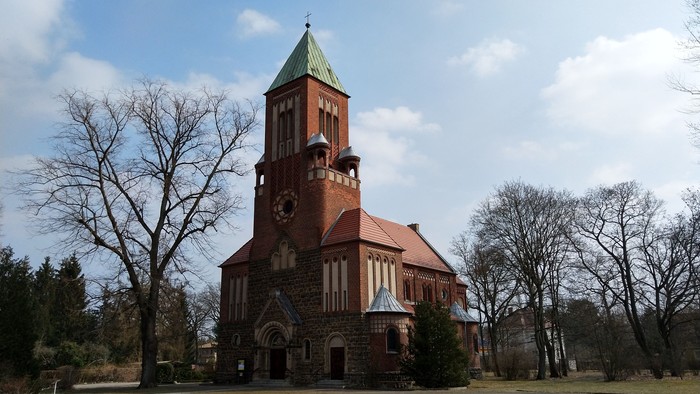 Ein rotes Backsteingebäude mit Uhrturm und spitzem Dach in einem Park.