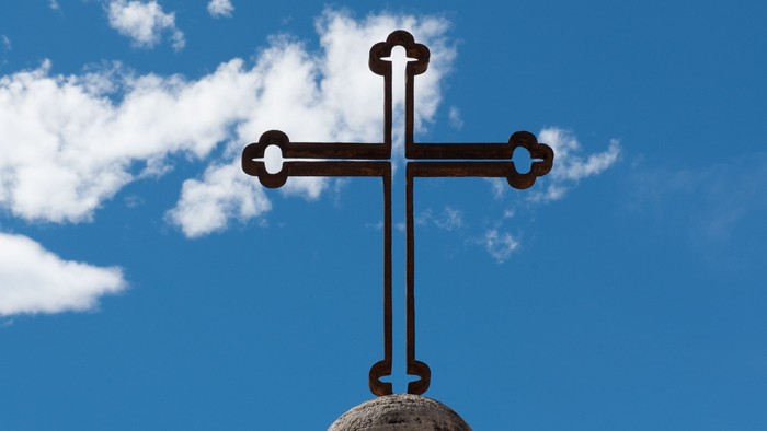 Kreuz auf einer Kuppel vor blauem Himmel mit weißen Wolken