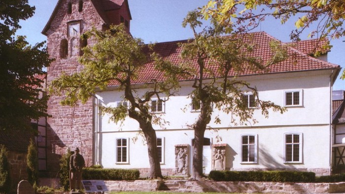 Großes weißes Gebäude mit rotem Dach und Uhrturm, umgeben von Bäumen und Grünflächen.