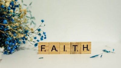 Wooden blocks spell out "FAITH" with blue flowers on a white surface.