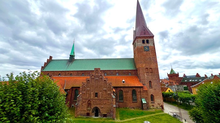 En stor kirke med spiret og grønne tag, omgivet af græs og buske