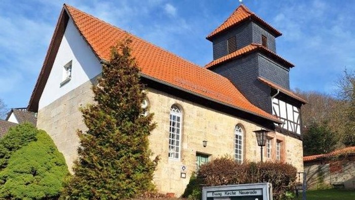 Kirche mit rotem Dach und Glockenturm, umgeben von Grünflächen und einer Steinmauer.