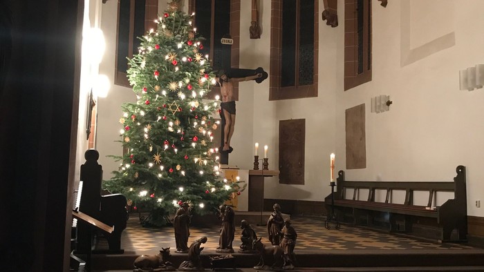 In der Kirche steht ein geschmückter Weihnachtsbaum, umgeben von Kerzen.