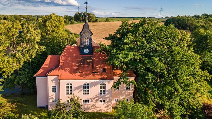 Weißes Gebäude mit rotem Dach und Uhrturm in ländlicher Umgebung