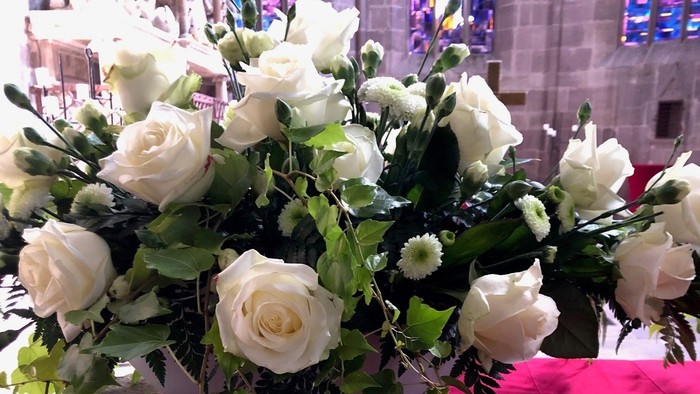 Elegante weiße Blumendekoration mit Rosen und Grünzeug auf einer roten Tischdecke in einer Kirche.