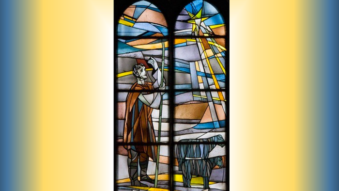 Buntglasfenster, das eine gewandete Figur mit einem Stab darstellt, mit abstraktem Hintergrund in Blau-, Gelb- und Brauntönen.