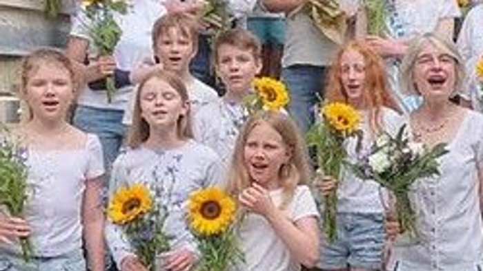 Eine Gruppe von Menschen, darunter Kinder und Erwachsene, posiert mit Sonnenblumen vor einem Gebäude.