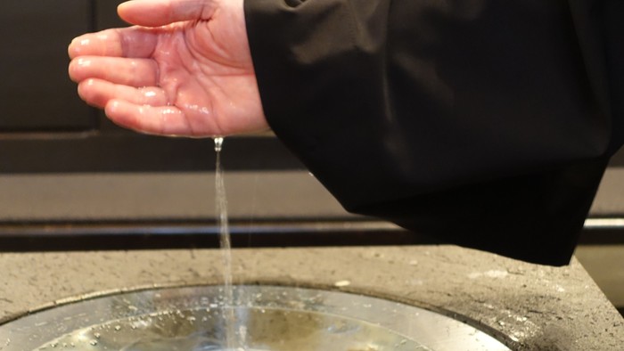 Person wäscht sich die Hände über einer Metallschale