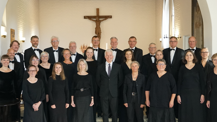 En kor med mænd og kvinder i formel klædning samlet i kirke med kors på baggrunden