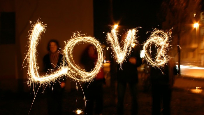 Personen schreiben mit Wunderkerzen das Wort "Liebe" in die Luft