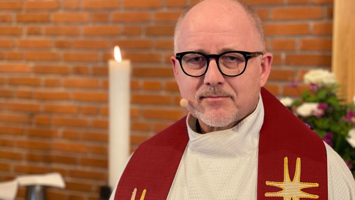 Mand i religiøs tøj foran murvæg og lysende stearinlys