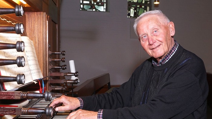 Ein älterer Mann spielt Klavier neben einem Weinregal.