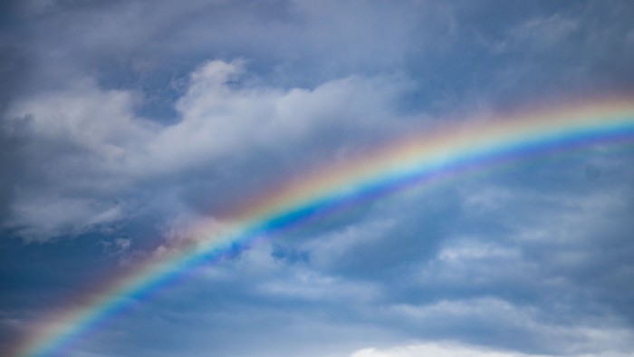 Ein lebendiger Regenbogen wölbt sich durch einen teilweise bewölkten Himmel.