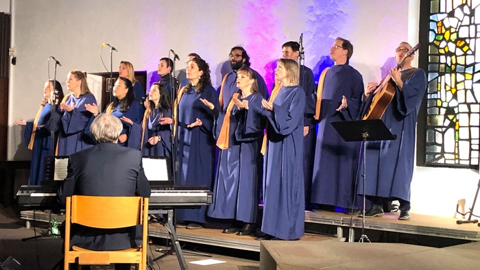 Ein Chor singt auf einer Bühne, begleitet von einem Pianisten.