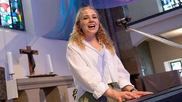 Eine Frau spielt Klavier in einer Kirche und lacht dabei.