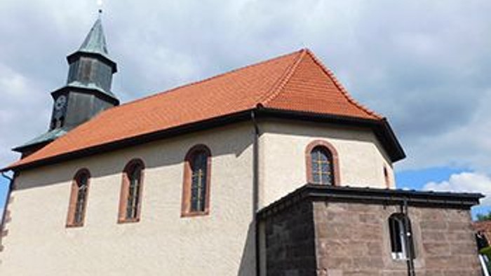 Kleine Kirche mit rotem Dach und Turm, umgeben von Wolkenhimmel
