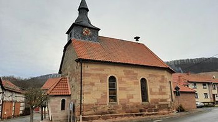 Kleine Kirche mit hohem Turm und rotem Dach in ländlicher Umgebung
