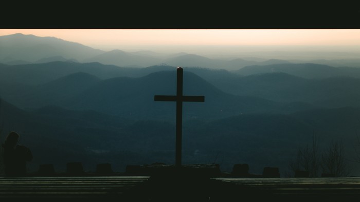 Ein Kreuz vor einem Bergpanorama bei Dämmerung
