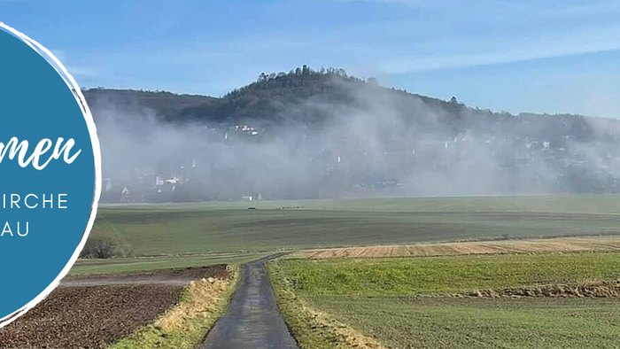 Willkommen in der **Evangelischen Kirche im Chattengau**, eingebettet in eine friedvolle Landschaft mit sanften Hügeln und Nebel.