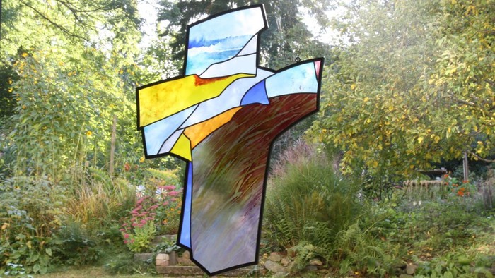 Bunter Glasfensterkreuz in Garten mit Bäumen und Büschen