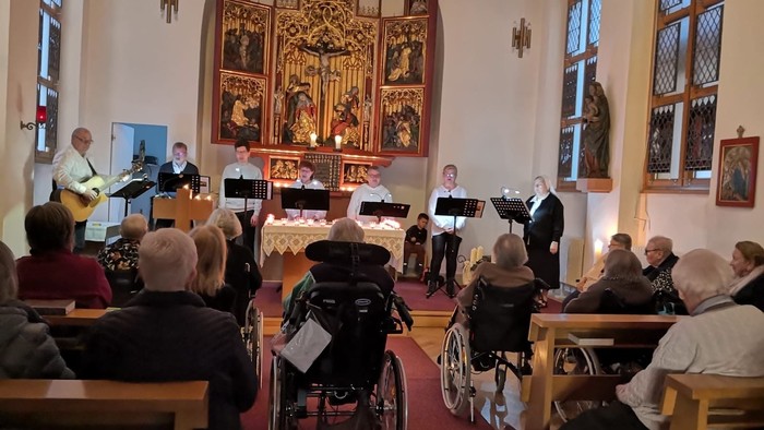 In der Kirche singt ein Chor, während das Publikum, darunter Rollstuhlfahrer, zuhört.