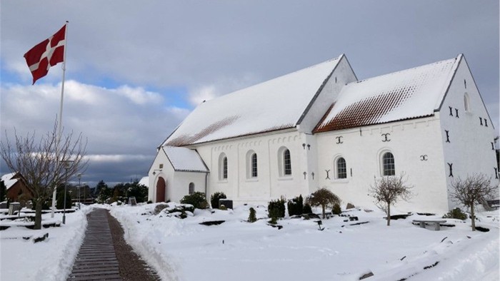 En snedækket kirke med dansk flag ved indgangen