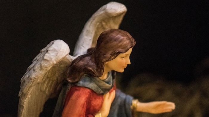 Englefigur i rød kjole, knælende på hø.