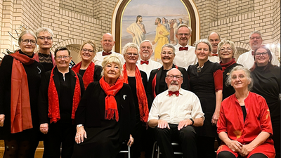 Gruppe af mennesker, der poser sammen, nogle iført røde halstørklæder, foran et religiøst vægmaleri.